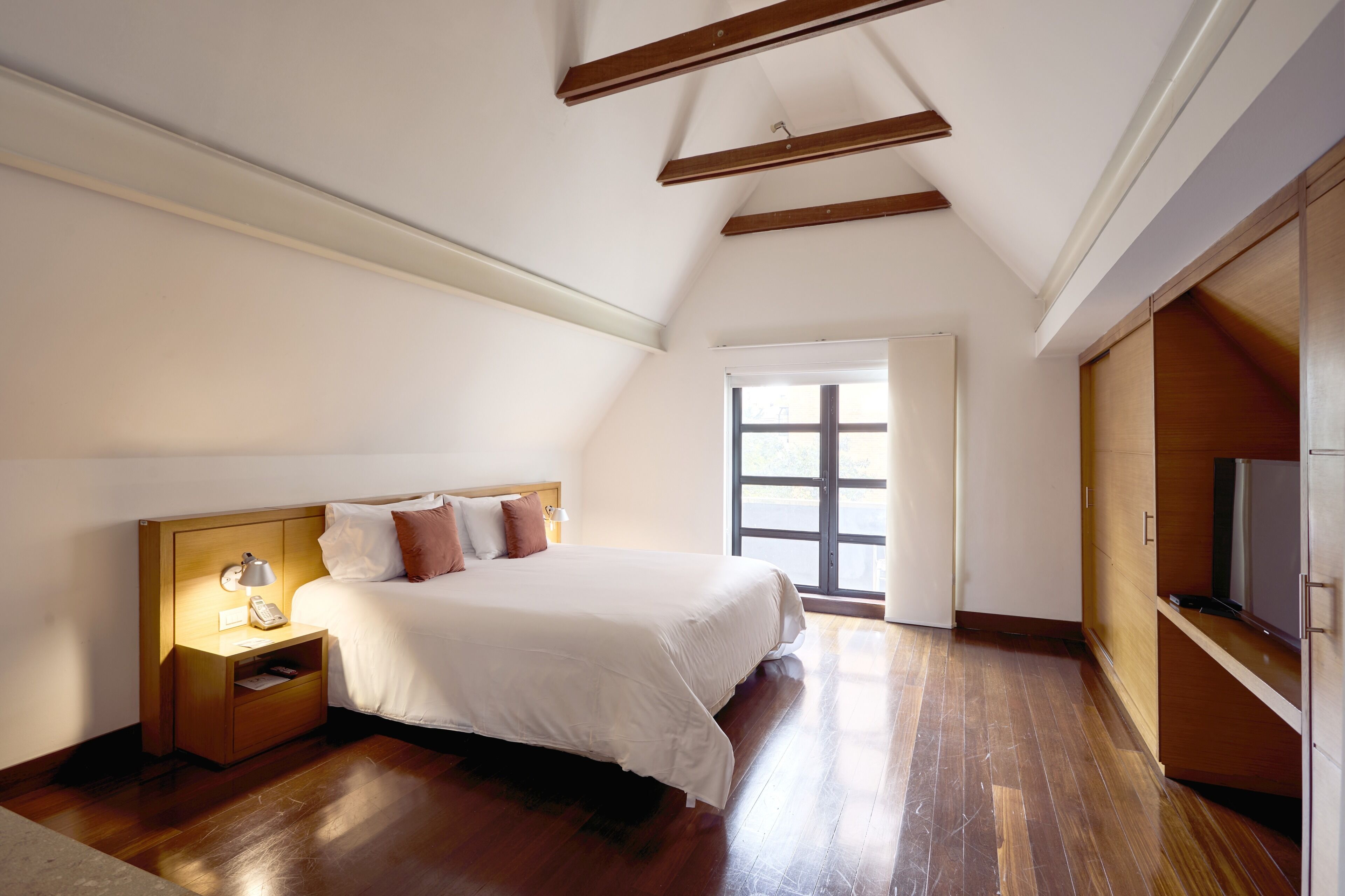 A bedroom with a bed, bedside table, lamp, and a window.