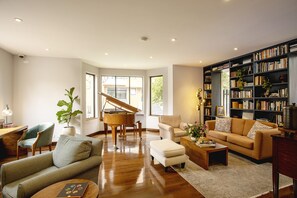 Una sala de estar espaciosa con un piano de cola, un conjunto de sofás acogedor, una mesa de centro y una estantería llena de libros.