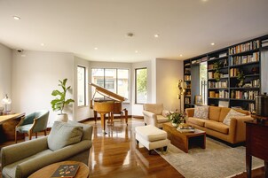 A spacious living room with a grand piano, a cozy sofa set, a coffee table, and a bookshelf filled with books.
