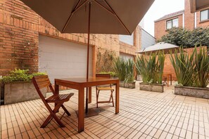 Eine Terrasse im Freien mit Holztisch und -stühlen, einem großen Sonnenschirm und Blumentöpfen.