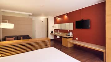 A modern hotel room with a bed, a desk, a TV, and a bathroom.