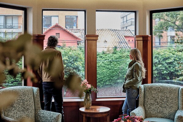 A room with large windows, a vase with flowers, and two chairs. - Bh la Quinta- Suites (Bogotá)