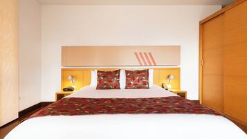 A hotel room with a large bed, two bedside tables with lamps, a wooden wardrobe, and a wall-mounted light fixture.