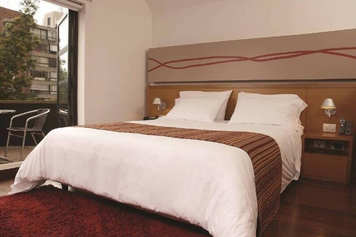 Ein Hotelzimmer mit Bett, Nachttisch, Sessel und Blick ins Freie.