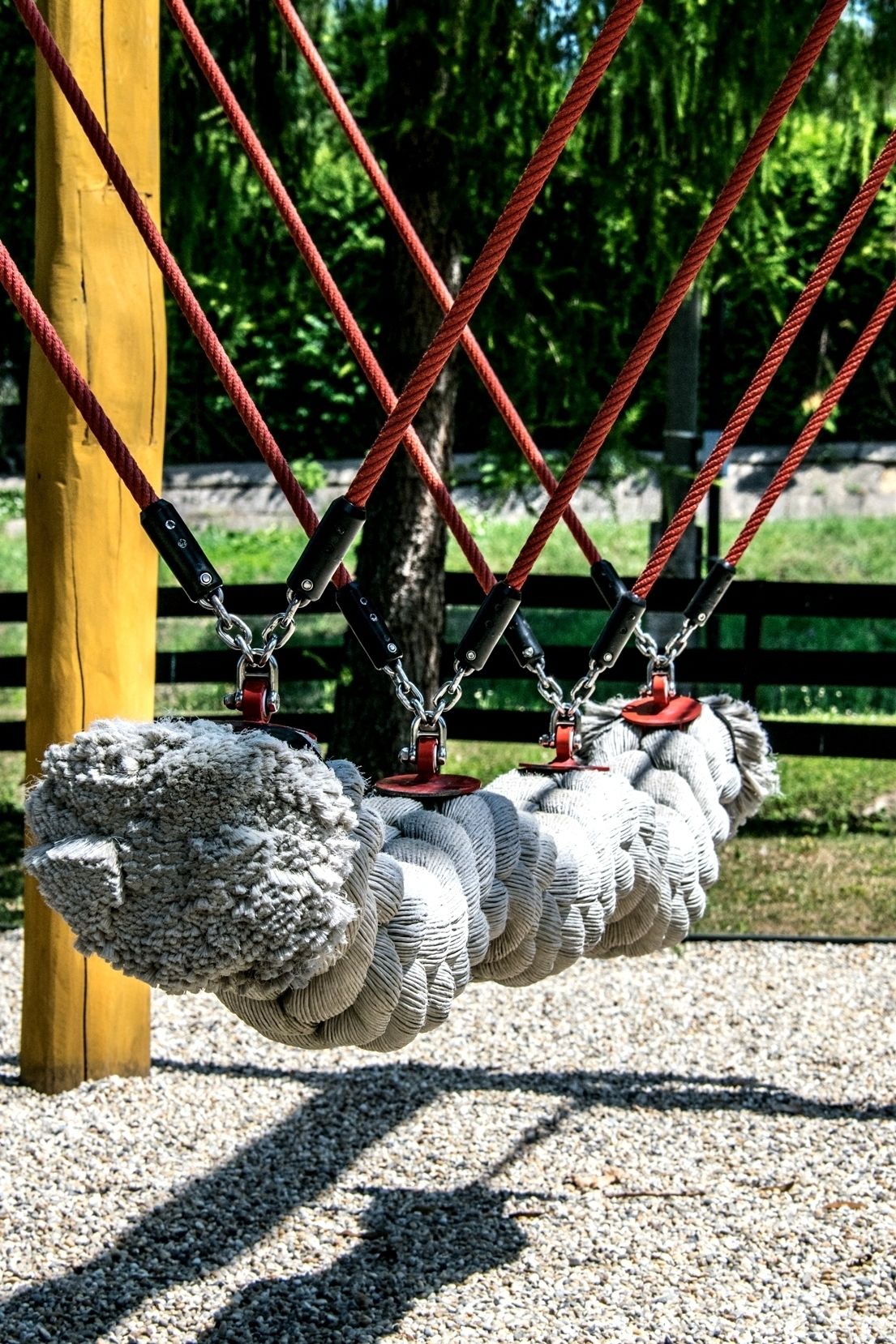 A swing set with red ropes and black metal chains, suspended from a yellow wooden post.