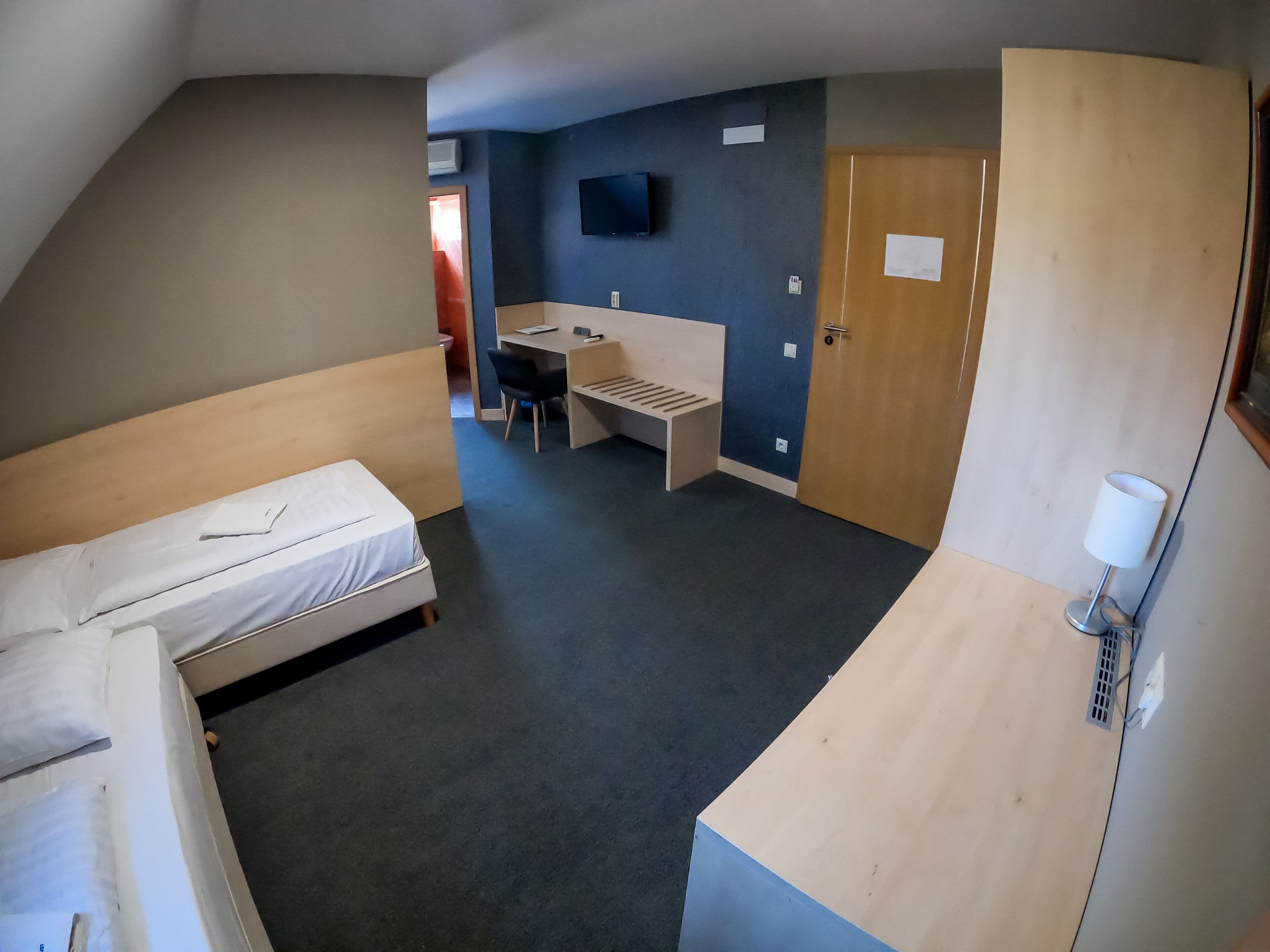 A compact hotel room with a bed, a desk, a chair, and a TV on the wall.