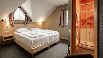 A bedroom with two beds, a window with curtains, a bedside table, and a shower room with a glass door.