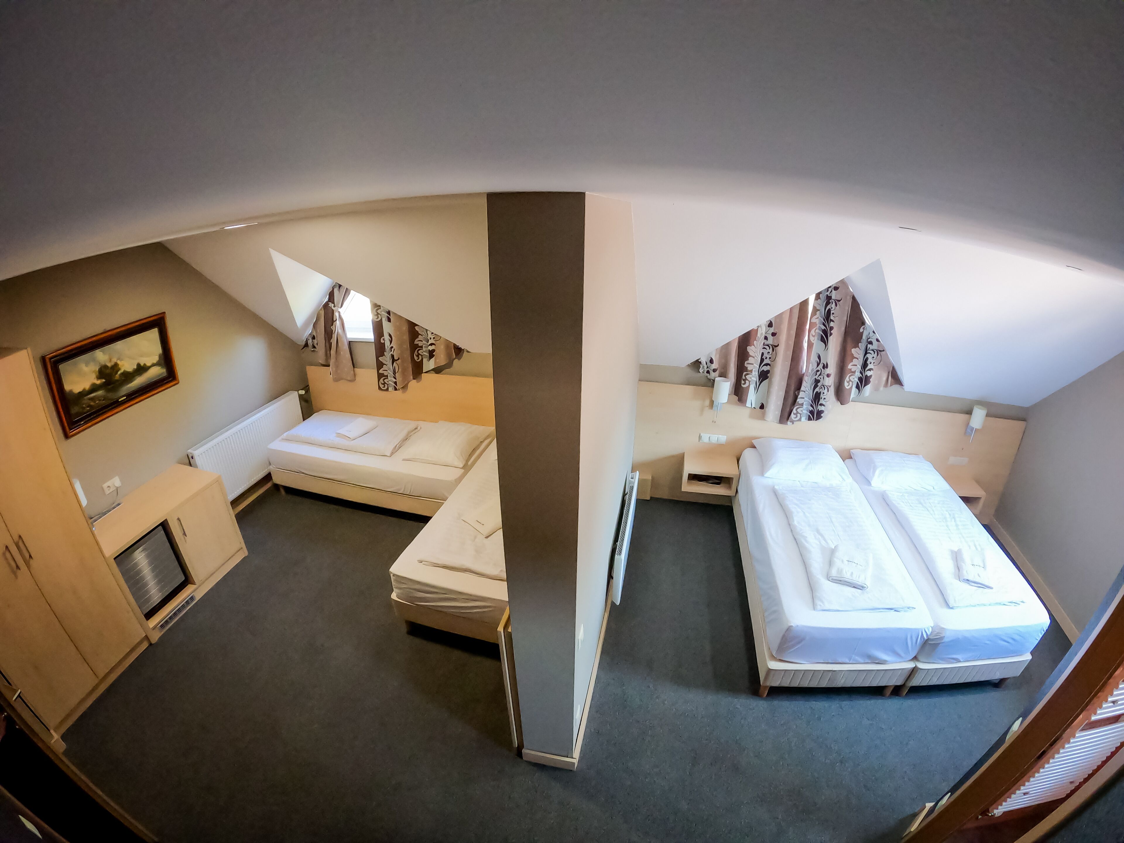 A hotel room with two single beds, a small desk, a radiator, and a television on the wall.