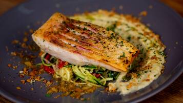 Un plato con un trozo de pescado, verduras y salsa cremosa.