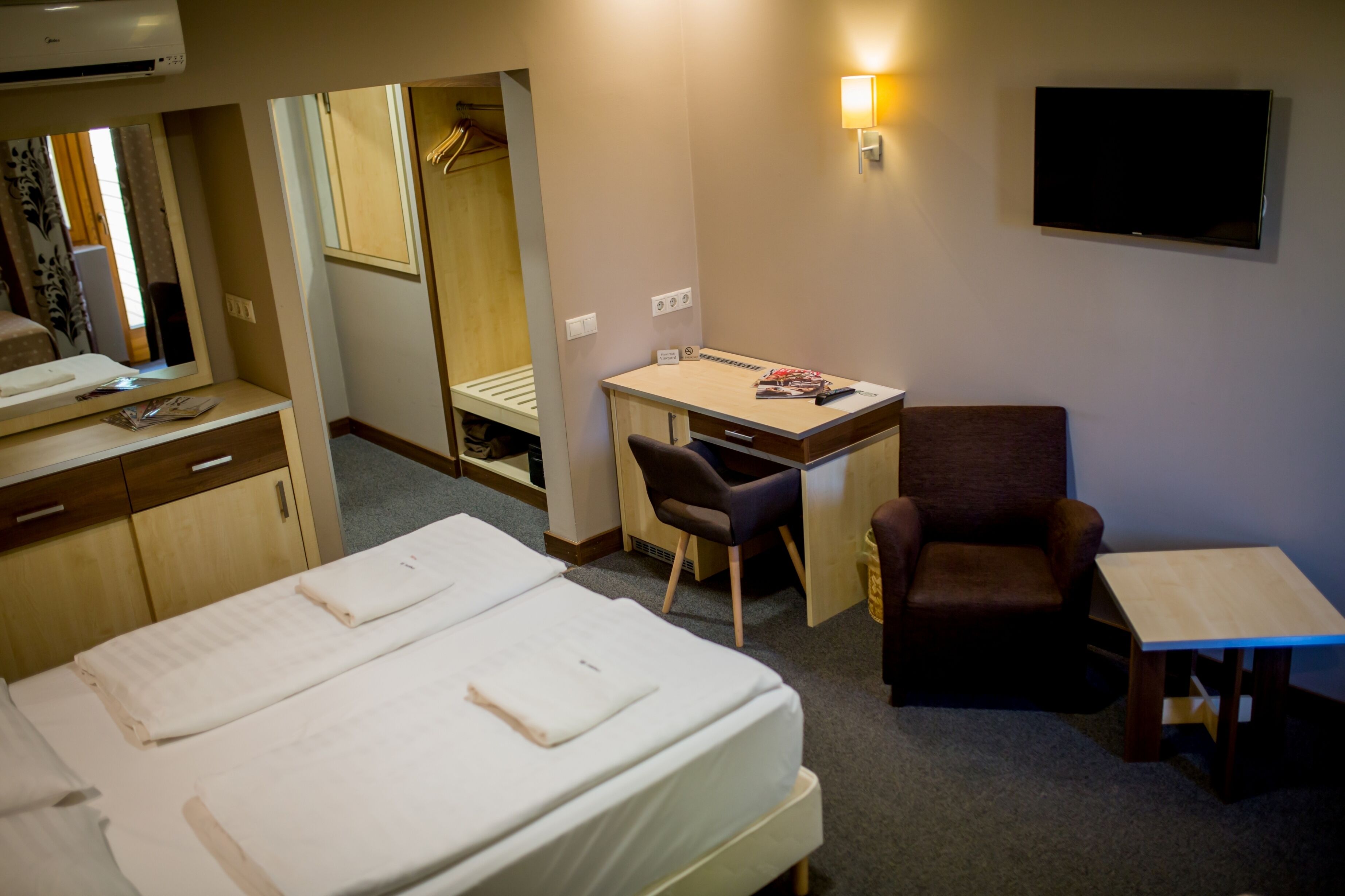 Ett hotellrum med två sängar, ett skrivbord, en stol, en TV och en garderob.