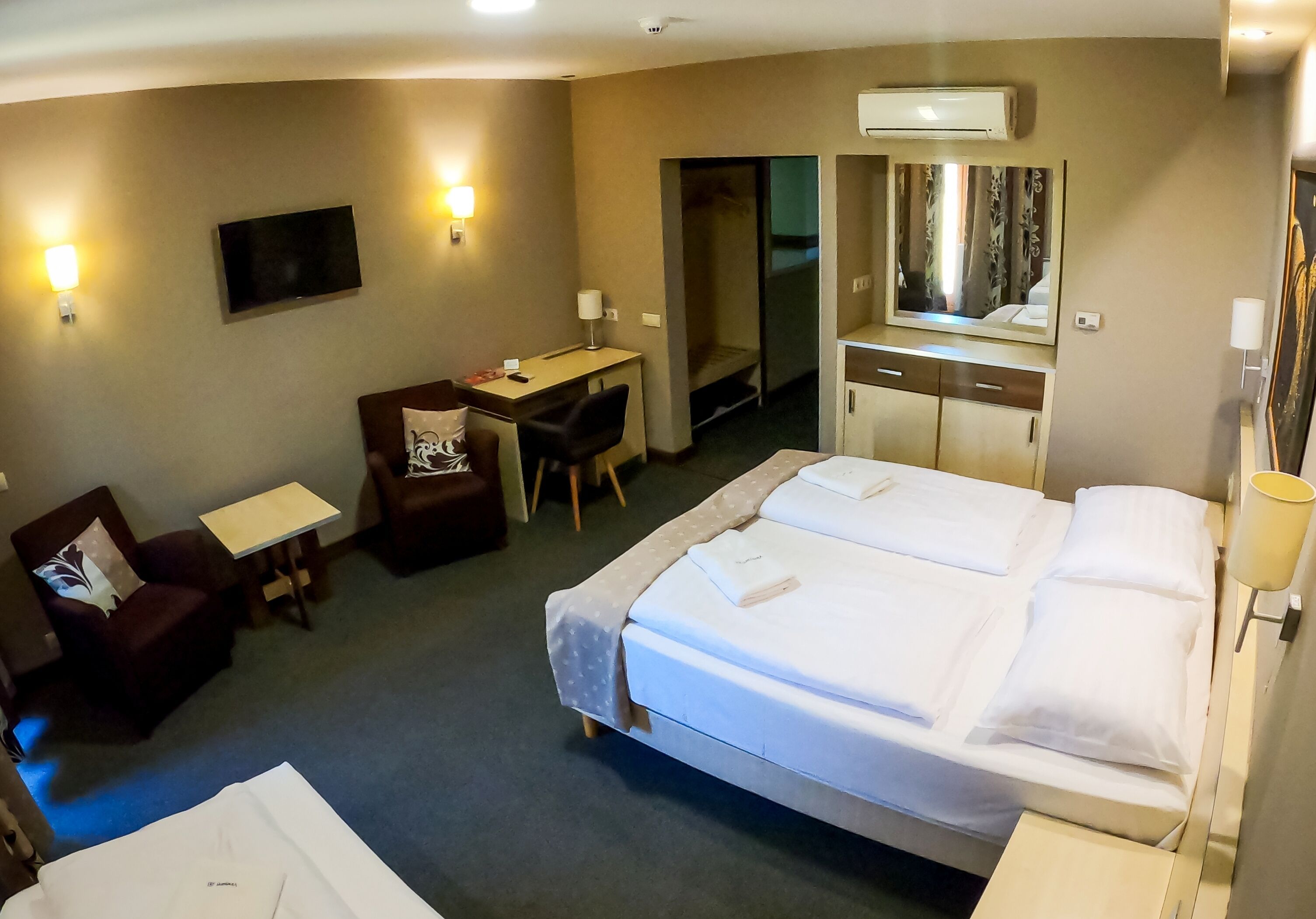 Ein Hotelzimmer mit einem großen Bett, einem Schreibtisch, einem Sessel, einem Fernseher und einem Spiegel.