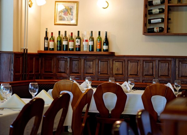Interior de restaurante con paneles de madera, una estantería para vinos en la pared y mesas con sillas ordenadas.