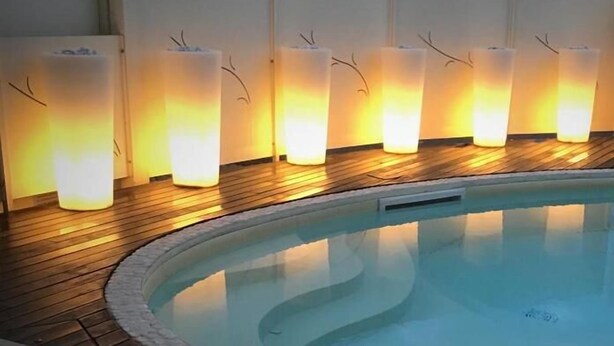 A swimming pool with a wooden deck and a row of illuminated wall sconces. - Resort del Lago (Desenzano del Garda)