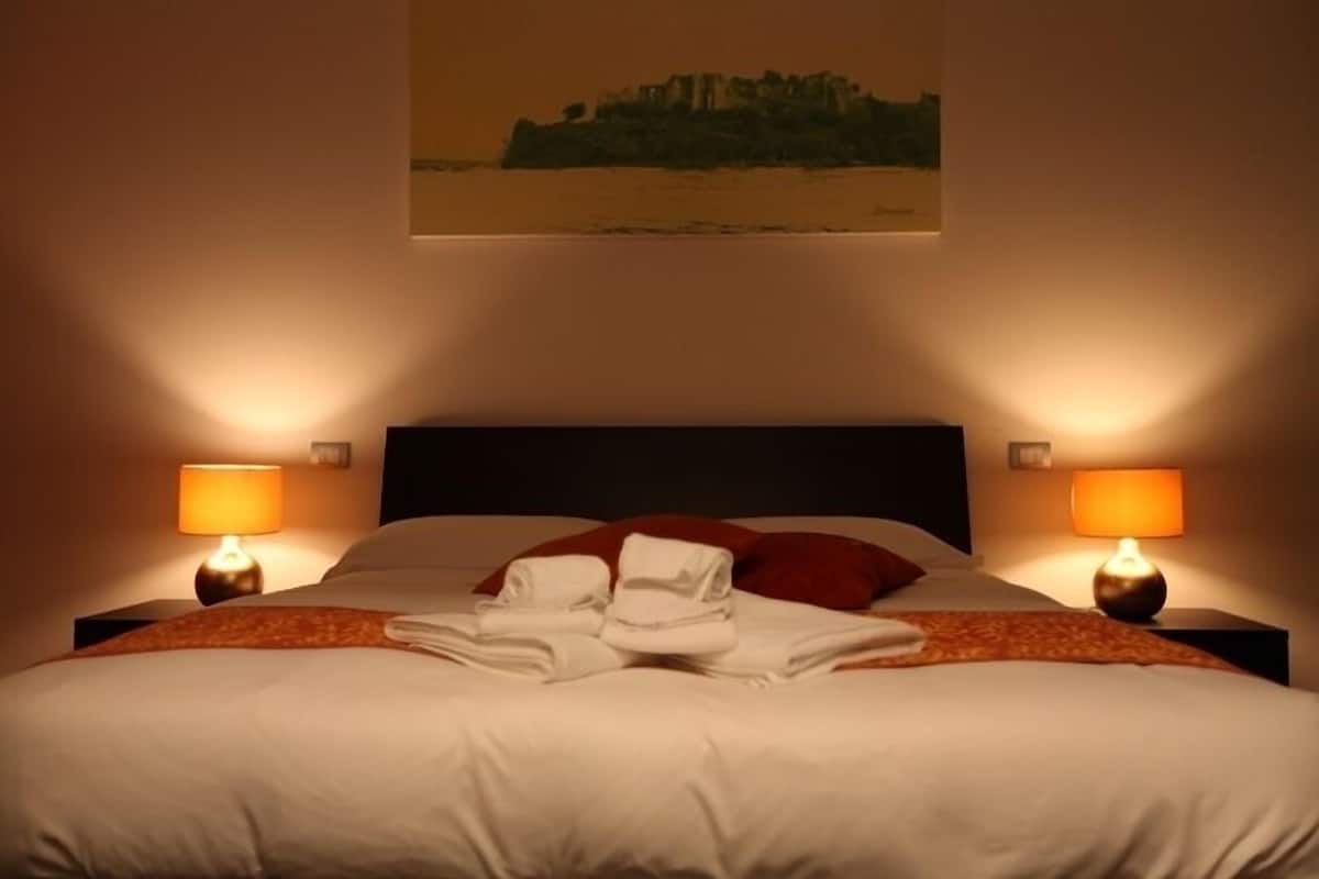 Una camera d'albergo con un letto grande, due lampade sui comodini, un cuscino rosso e un asciugamano sul letto.