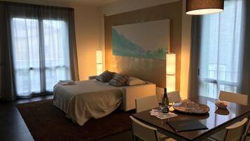 Une chambre d’hôtel comprenant un lit, une table de chevet, une lampe et une table à manger avec des chaises.