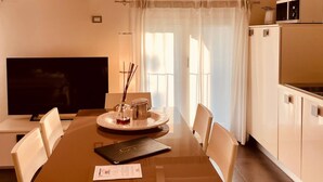 A dining area with a wooden table, chairs, a television, and a kitchen area with cabinets and a microwave. - Resort del Lago (Desenzano del Garda)