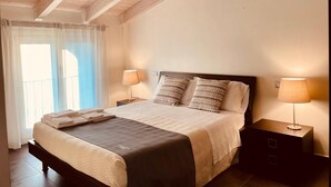 A bedroom with a bed, two bedside tables, a window with curtains, and a wooden ceiling. - Resort del Lago (Desenzano del Garda)