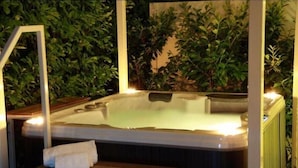 A hot tub with a wooden bench and a towel, surrounded by lush green plants. - Resort del Lago (Desenzano del Garda)