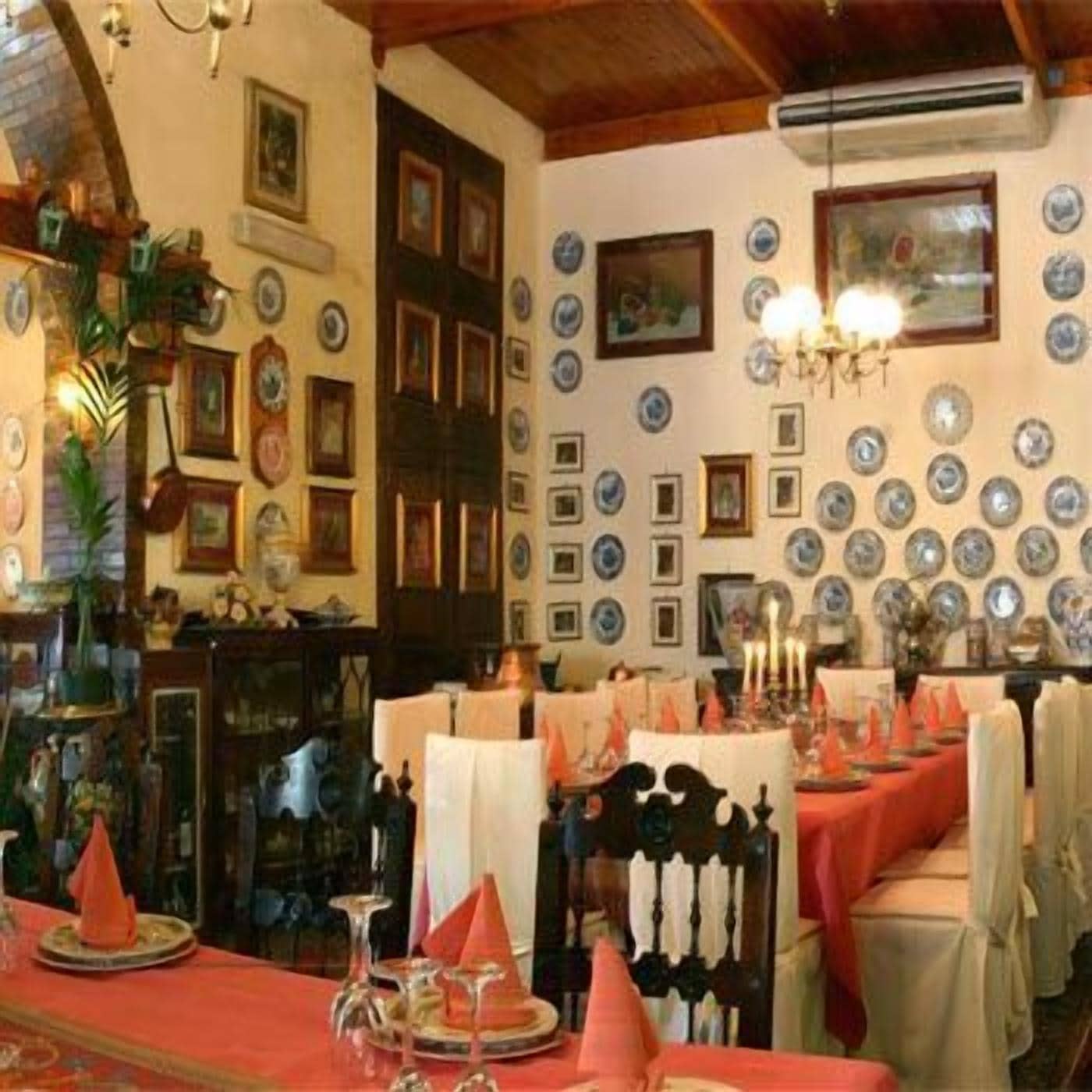 A dining area with a long table set for a meal, surrounded by walls adorned with numerous framed pictures and decorative plates.