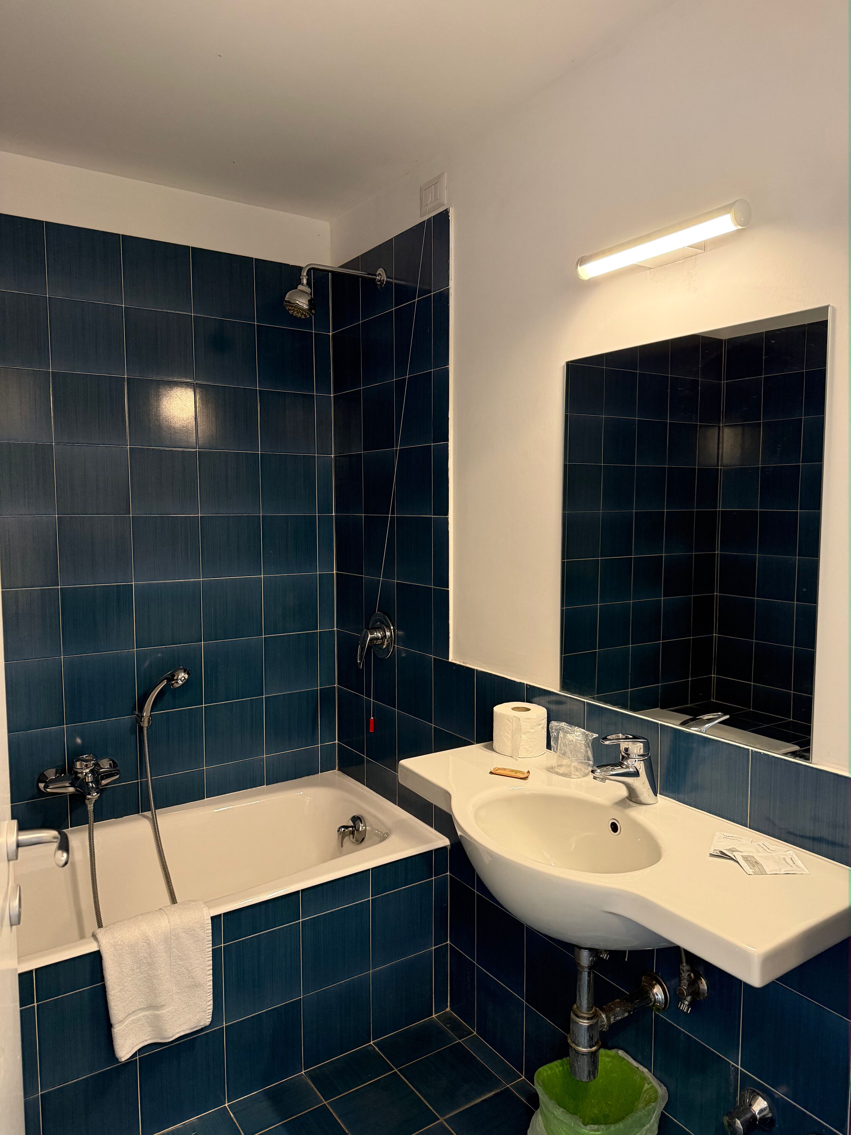 Een badkamer met donkerblauwe tegels, een witte badkuip, een witte wastafel en een spiegel boven de wastafel.