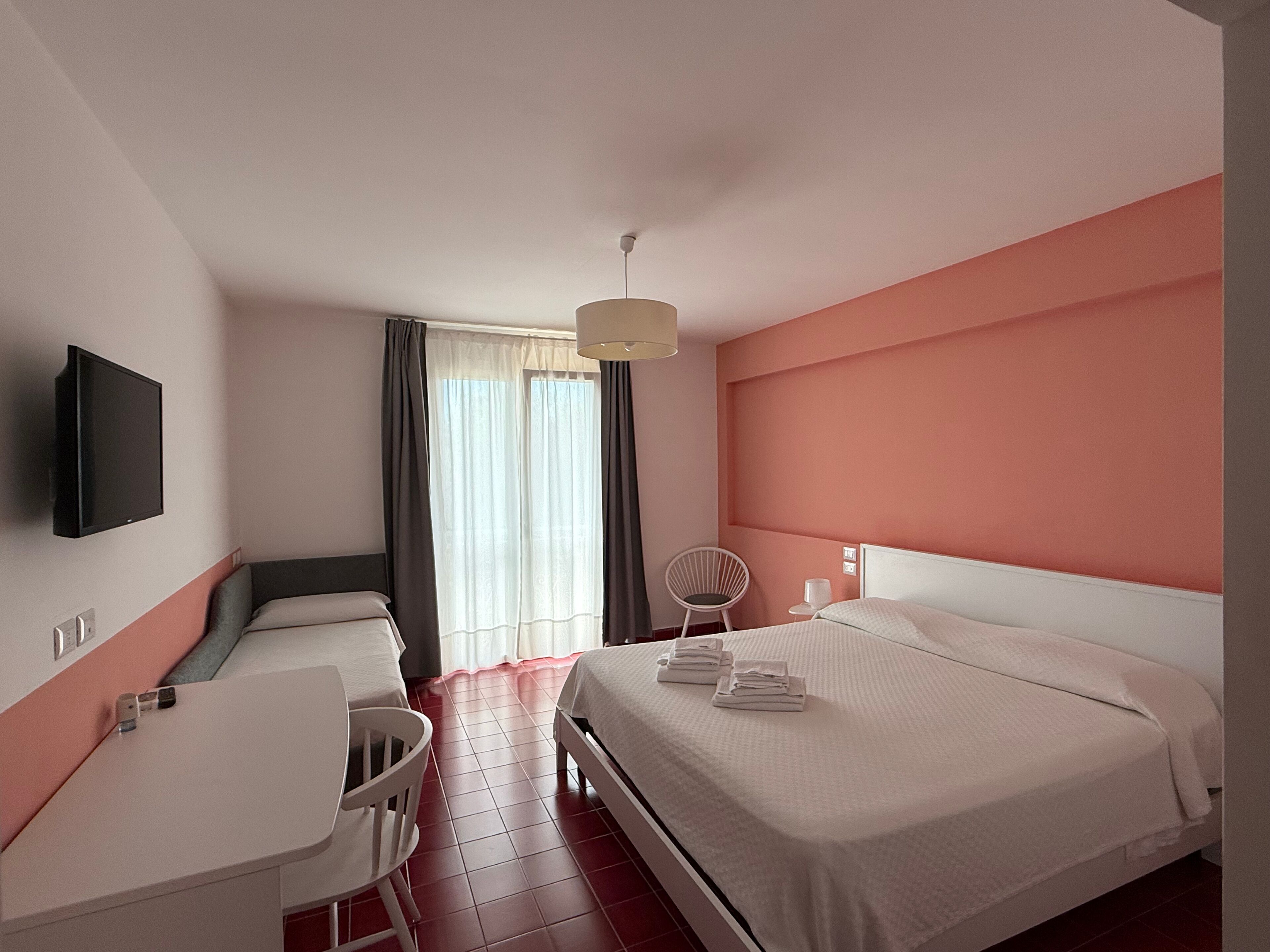 Une chambre d’hôtel équipée d’un lit, d’un bureau, d’une chaise, d’une télévision et d’une fenêtre avec des rideaux.