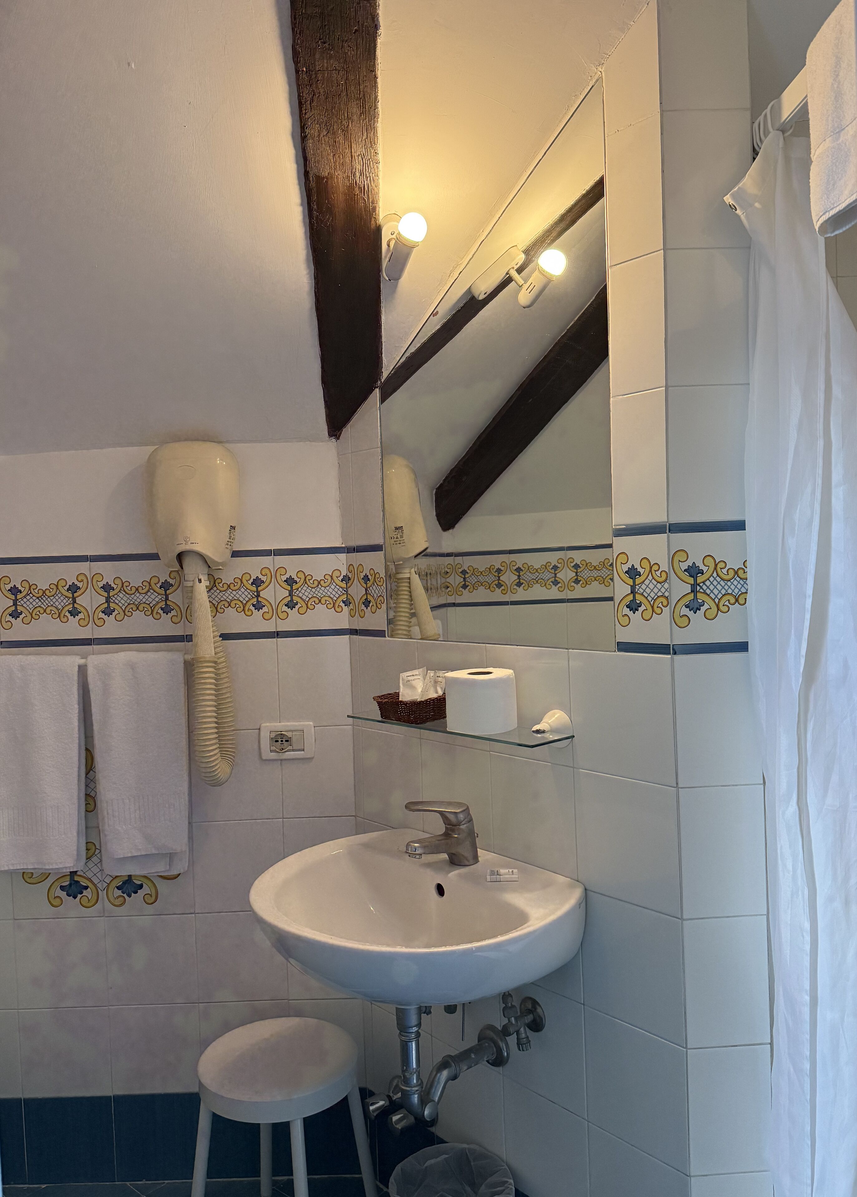 A bathroom with a white sink, a mirror, a towel rack, a hairdryer, and a shower curtain.