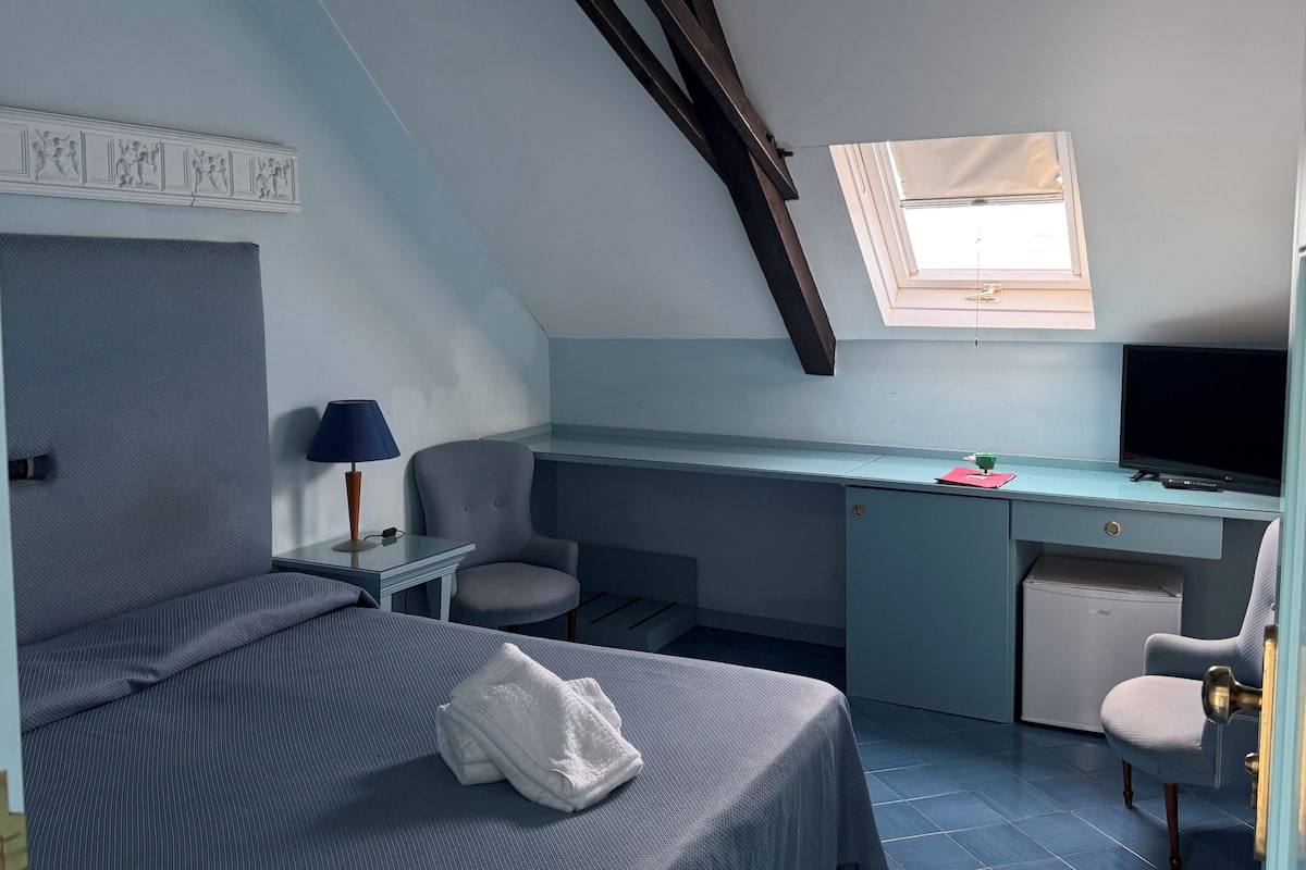 Ein Schlafzimmer mit einem Bett, einem Schreibtisch, einem Stuhl, einem Fernseher und einem kleinen Fenster.