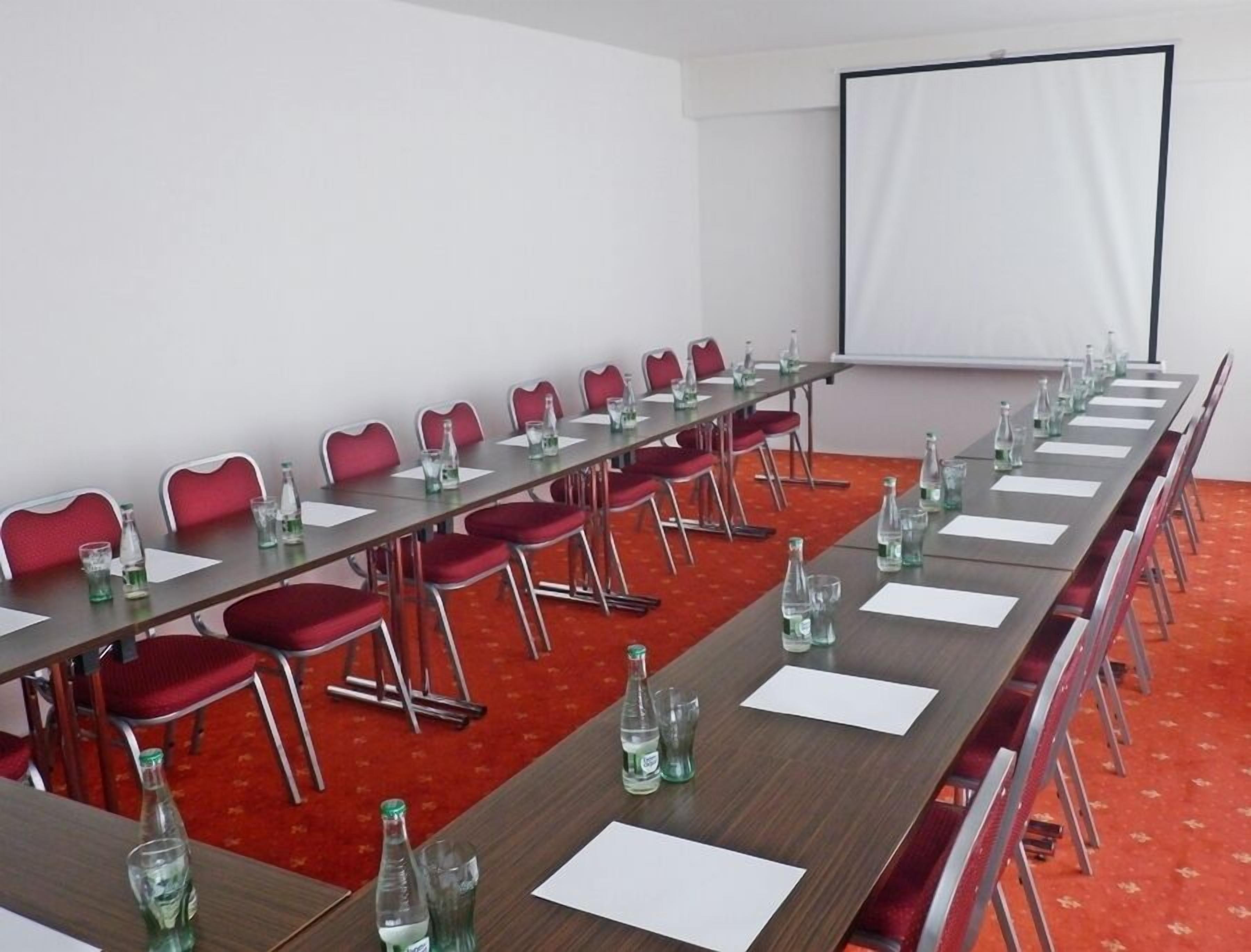 A conference room with a long table, red chairs, and a projector screen.
