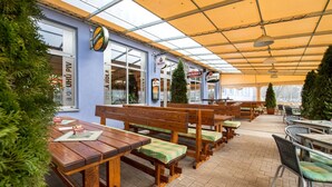 An outdoor seating area with wooden benches and tables, covered by a yellow canopy. - Alessandria (Hradec Kralove)