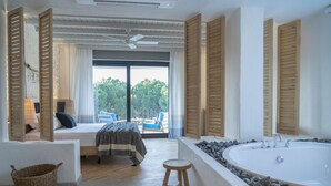 Une chambre à coucher avec un grand lit, un tabouret en bois, un panier en osier et une baignoire entourée de pierres.
