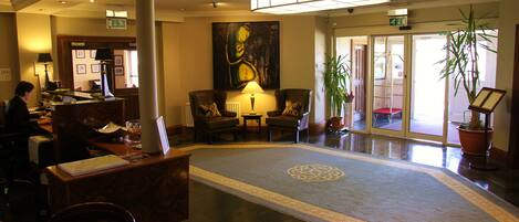 A lobby with a reception desk, seating area, artwork, and potted plants.