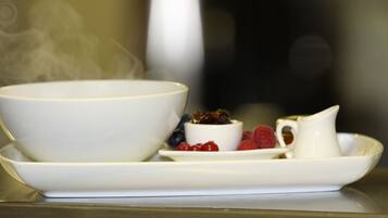 A white bowl, a small cup, and a pitcher on a white plate with berries and a slice of fruit.