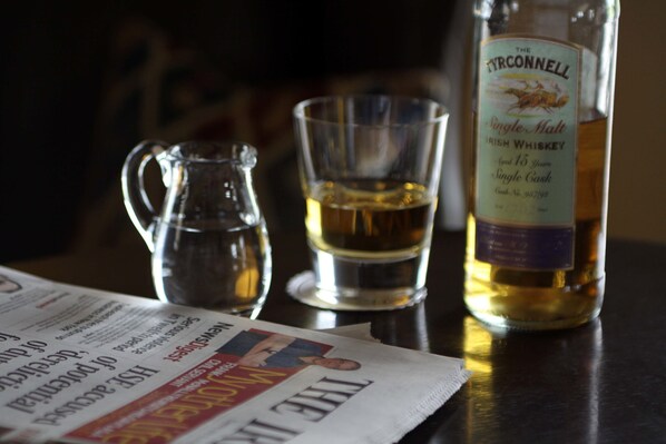 A bottle of The Tyrconnell Irish Whiskey, a glass pitcher, and a glass of whiskey on a table with a newspaper. - Vaughan Lodge Hotel (Lahinch)