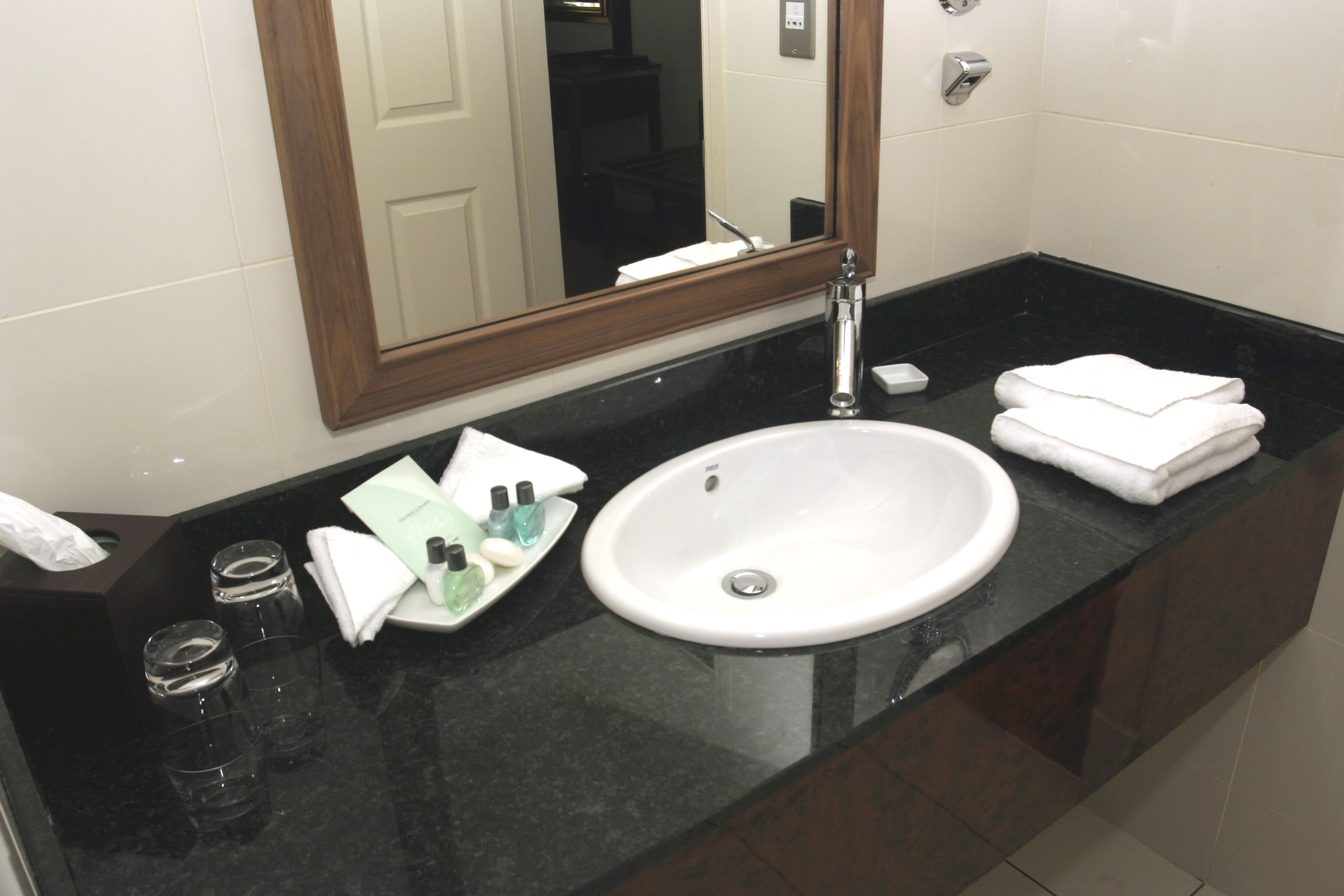 Un baño de hotel con un lavamanos blanco, un espejo y una encimera negra.