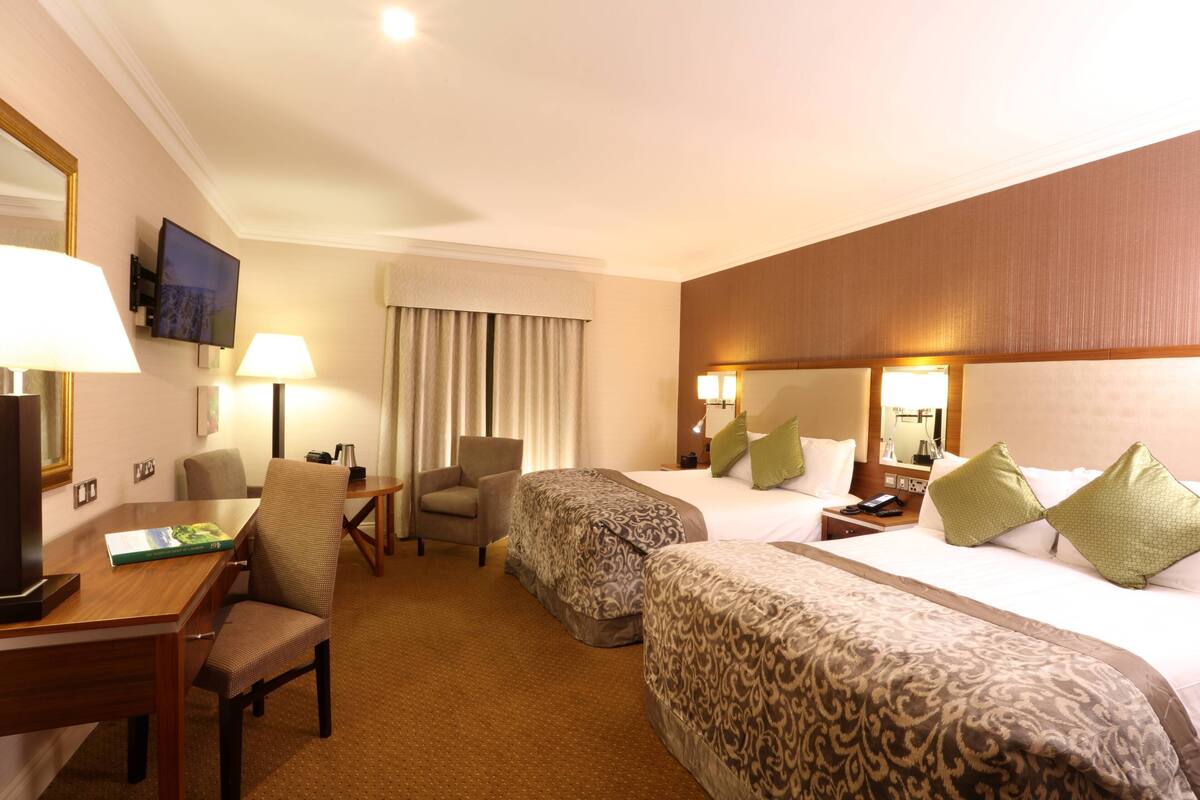 A hotel room with two beds, a desk, a chair, a TV, and a window with curtains.