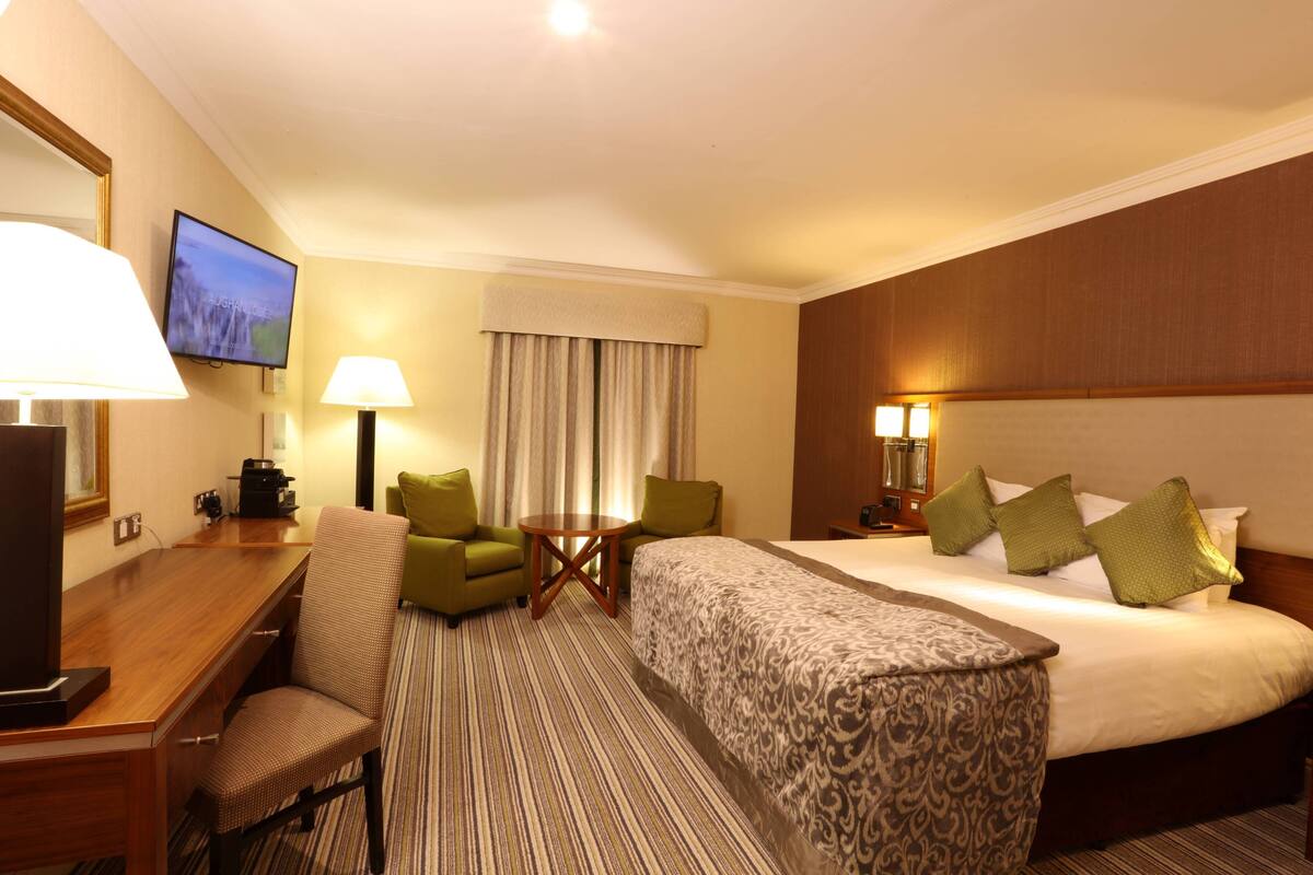 A hotel room with a large bed, a desk with a chair, a television, and a small table with lamps.