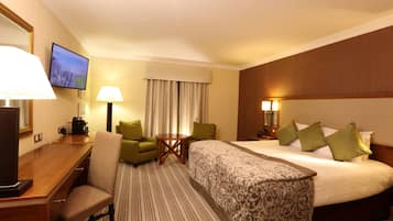 A hotel room with a large bed, a desk with a chair, a television, and a small table with lamps.