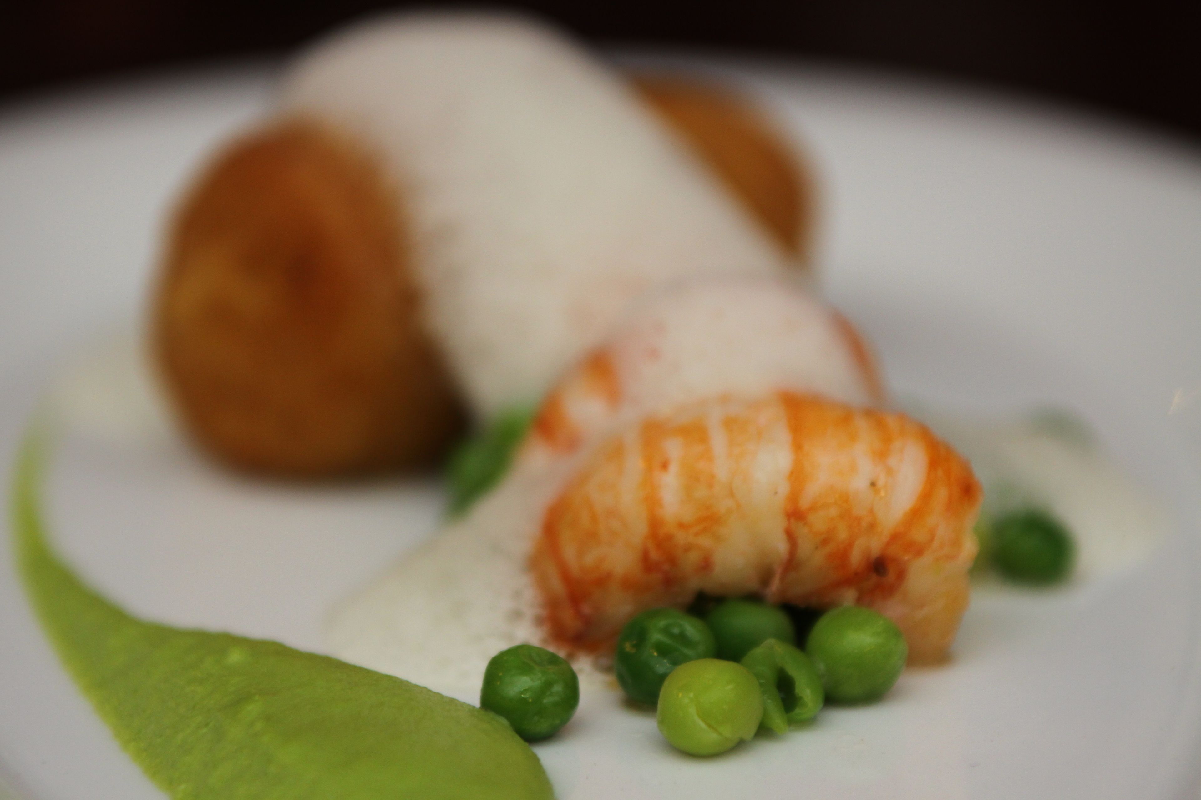 Un plato con un bocado de comida, guisantes y salsa verde.