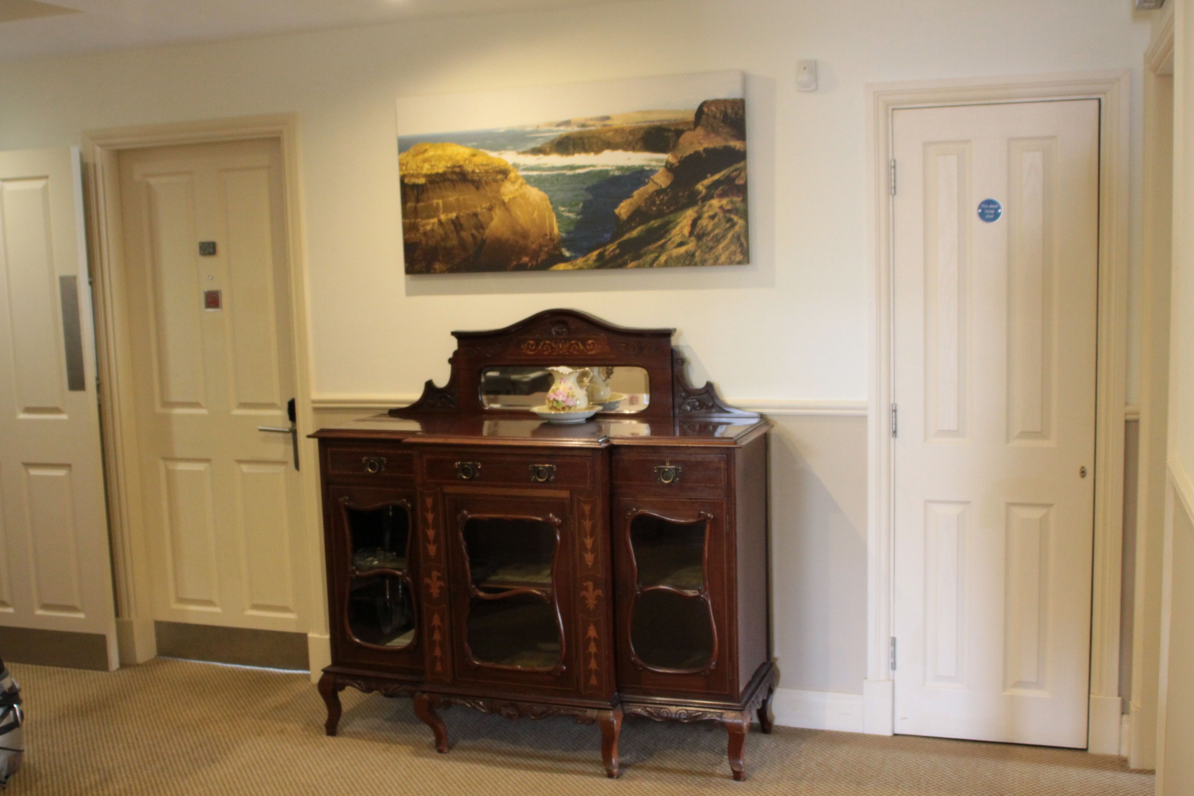 A room with a wooden cabinet, a painting of a coastal landscape, and white doors.