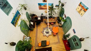A room with a patterned floor, a central table with chairs, a sofa, and various potted plants.