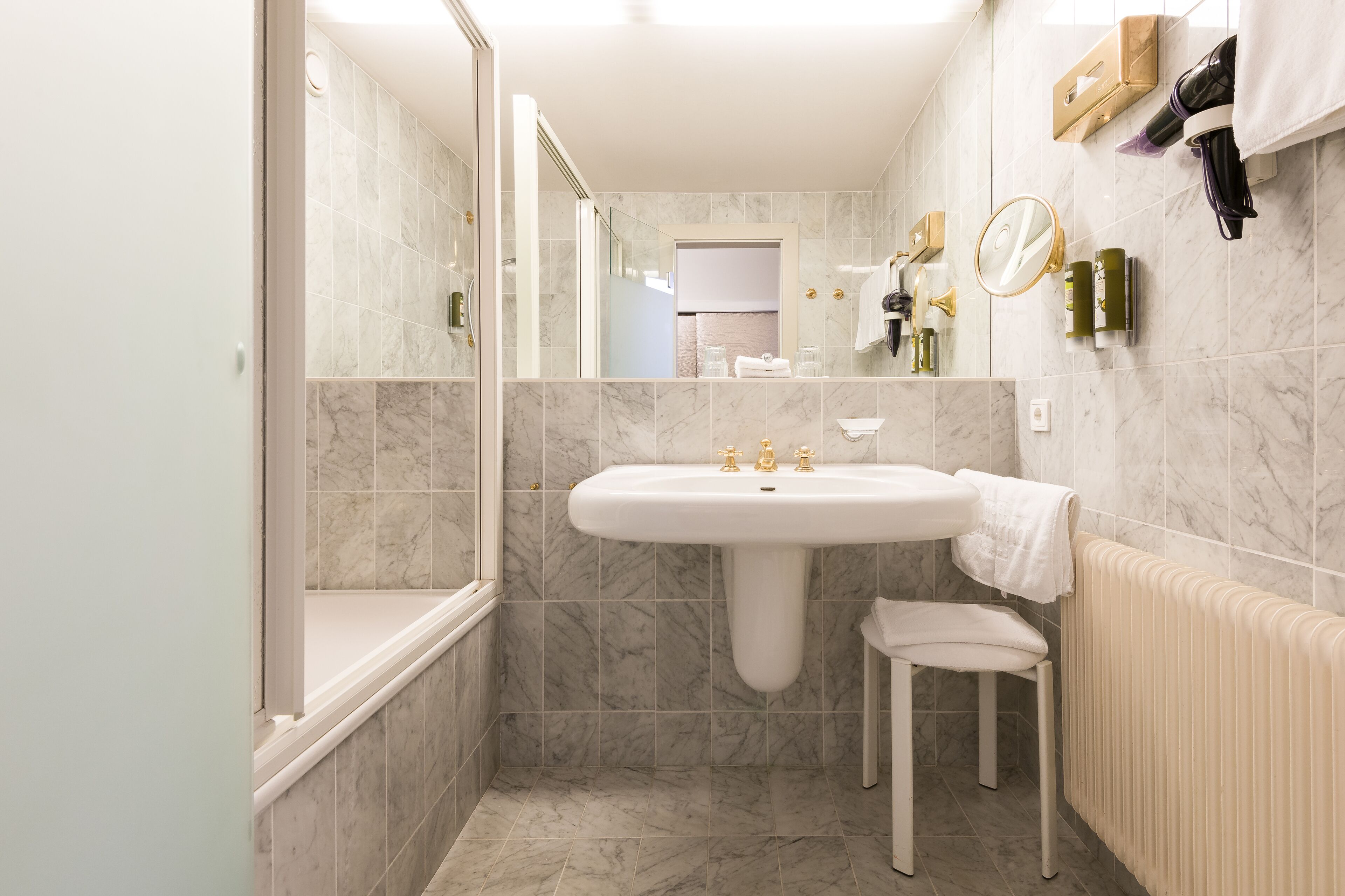 A modern bathroom with a marble sink, a glass shower enclosure, and a towel rack.