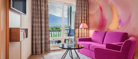 A modern living room with a pink sofa, a glass coffee table, and a view of mountains through large windows.