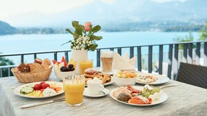 Una mesa de desayuno con diversas comidas y bebidas, con vistas a un lago y montañas al fondo.