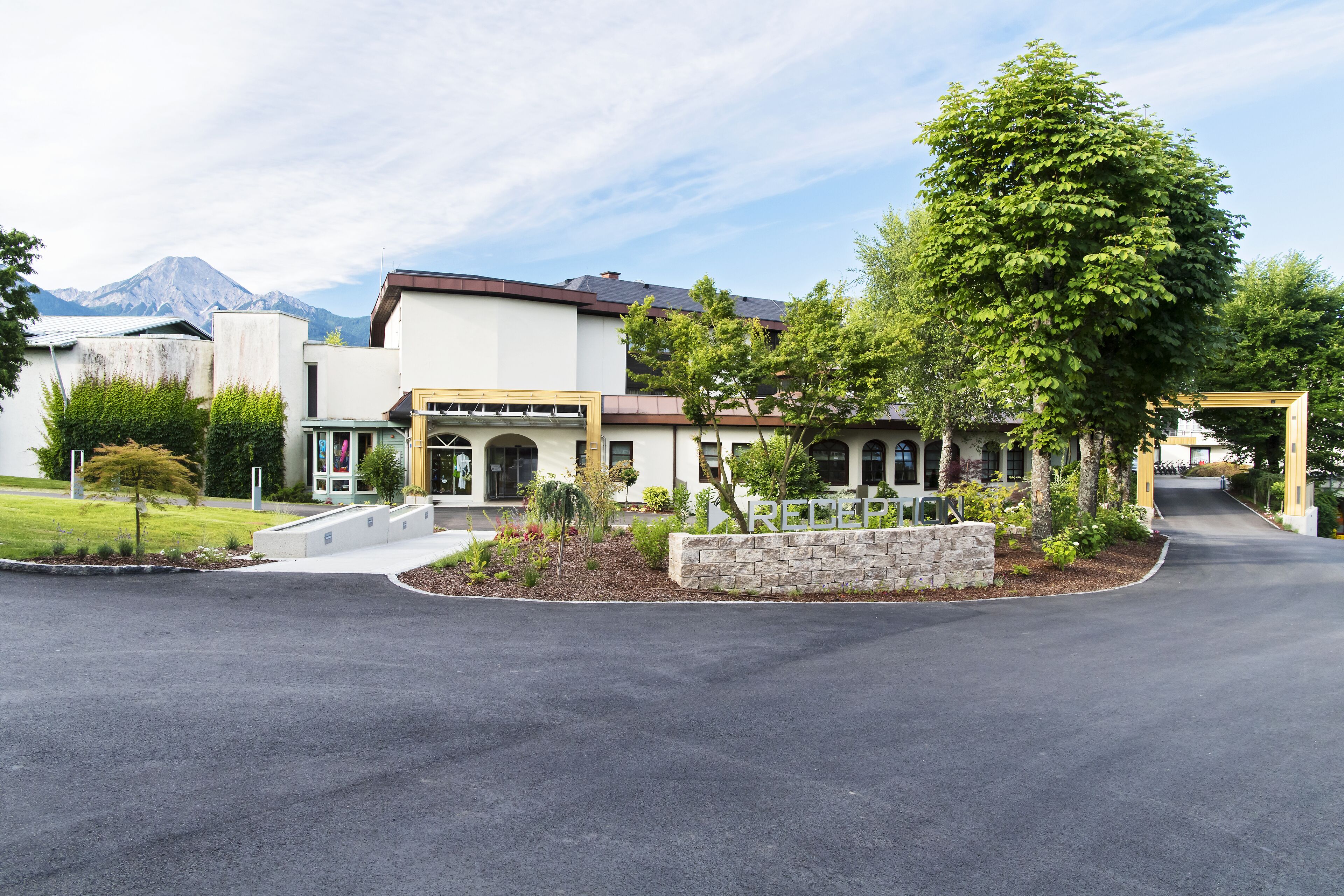 A modern building with a stone facade, a covered entrance, and a landscaped area with trees and shrubs.