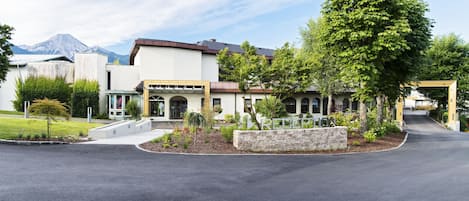 A modern building with a stone facade, a covered entrance, and a landscaped area with trees and shrubs.