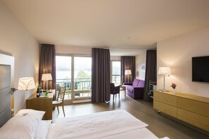 A hotel room with a bed, a desk with a lamp, a chair, a sofa, a TV, and a balcony with curtains. - Hotel Karnerhof (Villach)