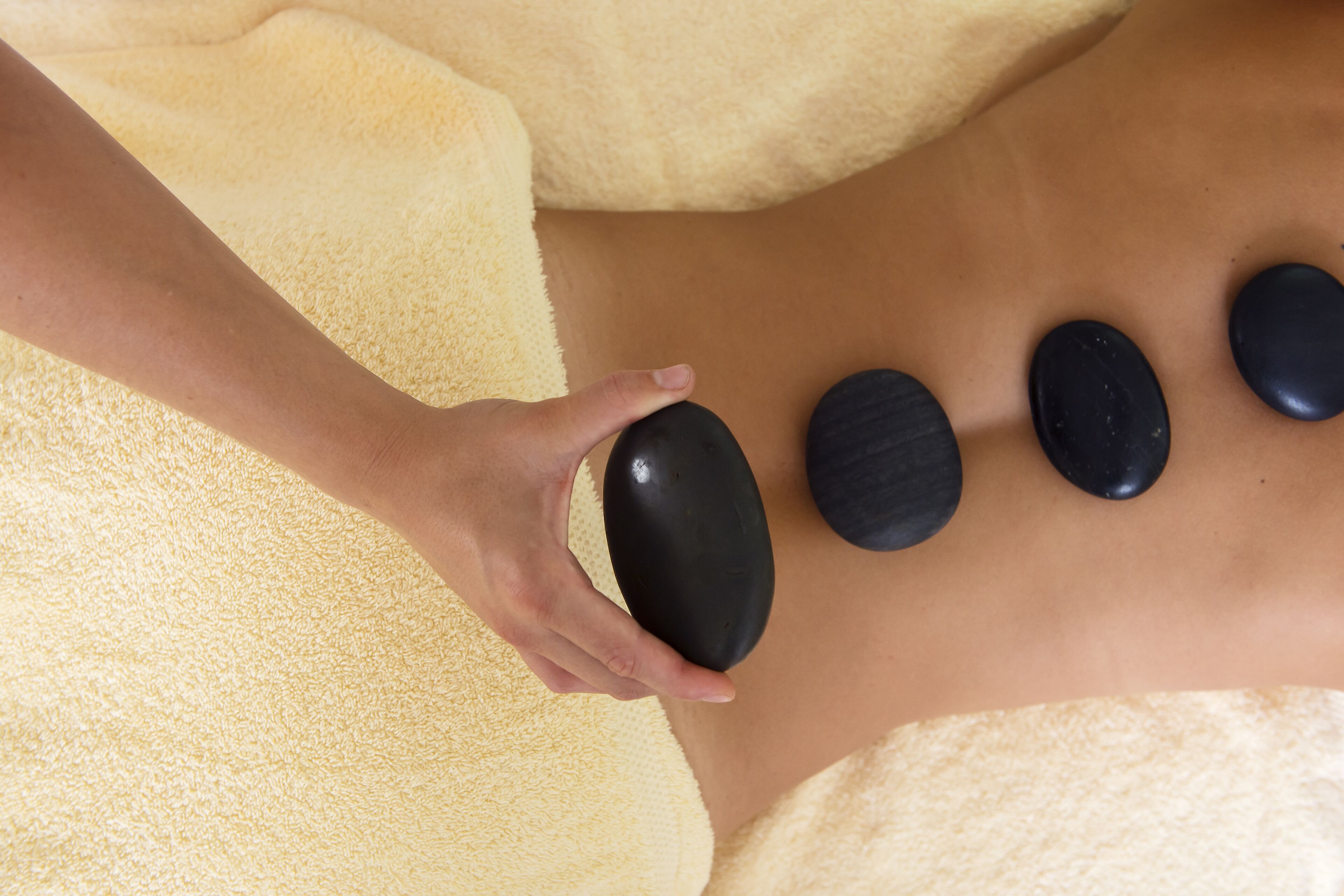 Eine Person erhält eine Steinmassage, wobei vier schwarze Steine auf dem Rücken platziert sind.