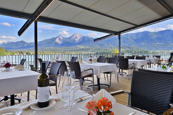 Un espace de restauration en plein air, avec des tables dressées pour le repas, offrant une vue sur un lac et des montagnes.