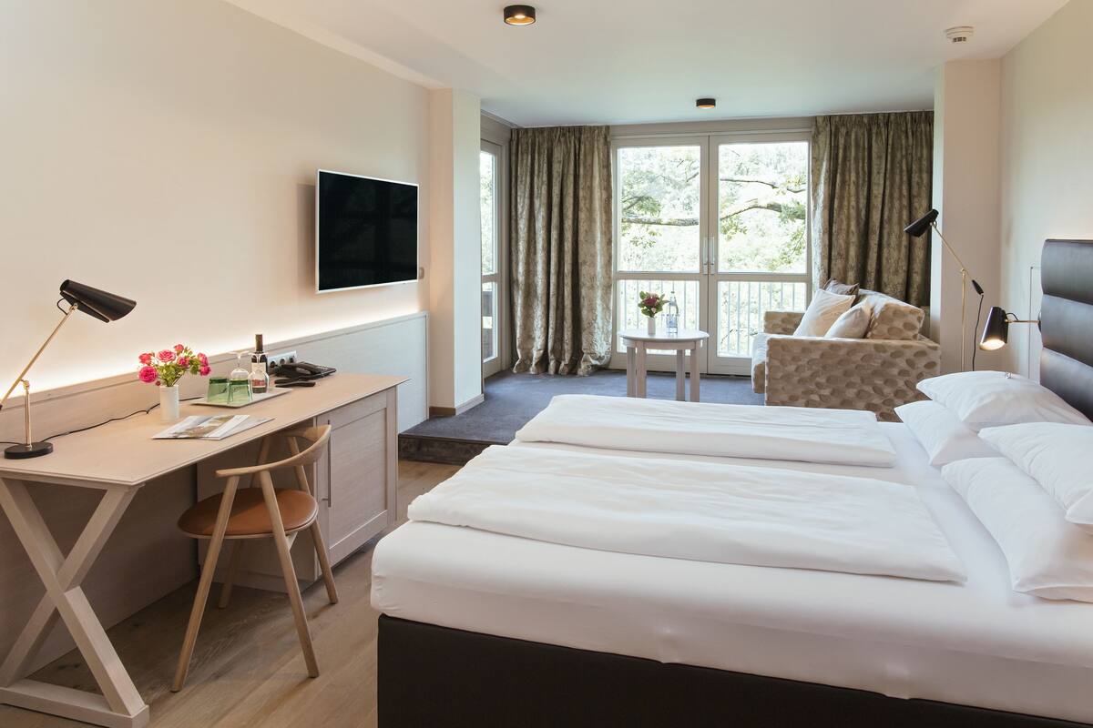 Habitación de hotel con cama, escritorio, silla, televisor y vistas al exterior.