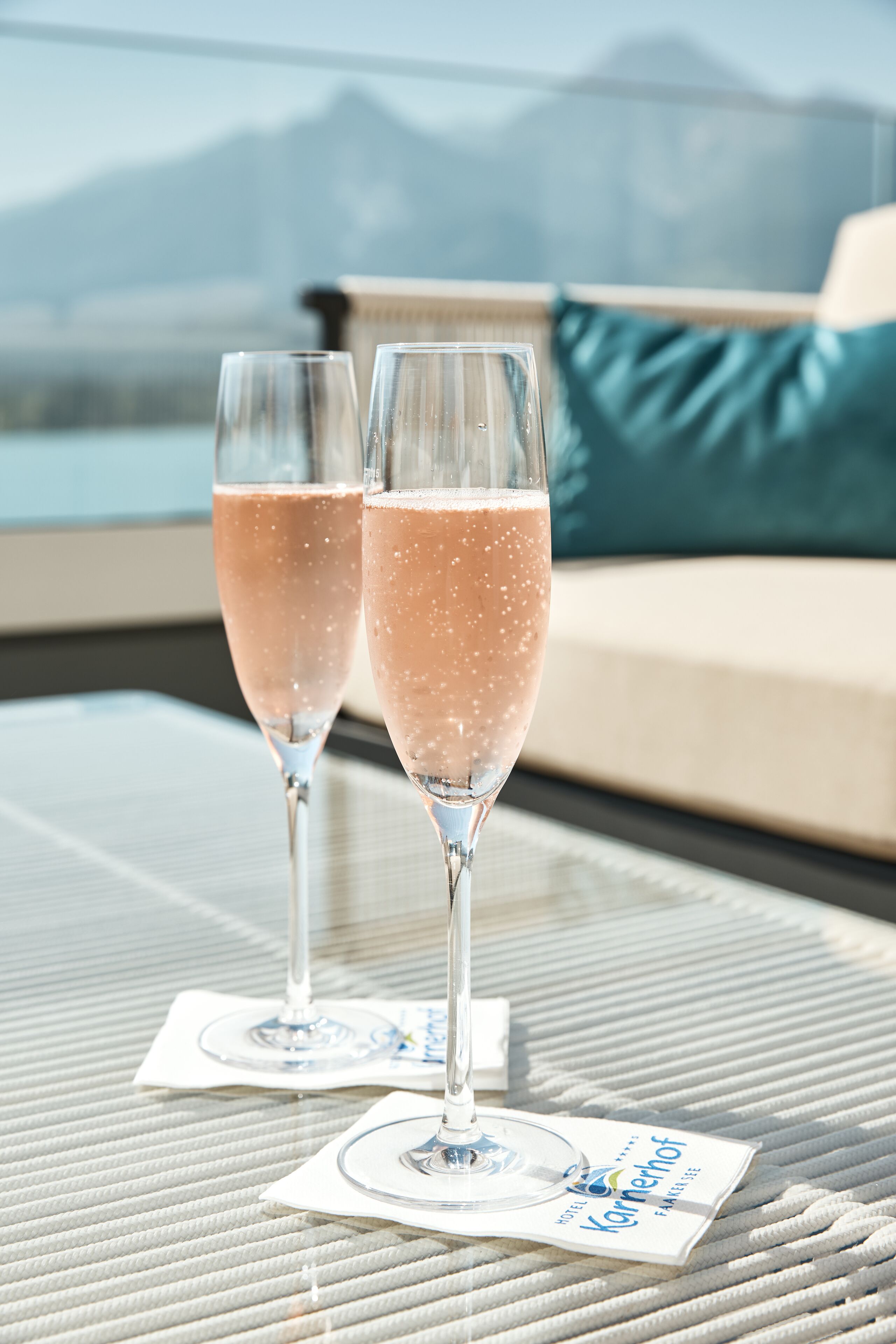 Two champagne glasses on a table with a view of mountains in the background.